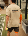 Model wearing Cuera Active Light Weight T-Shirt in Sand, lifestyle action shot on the padel court