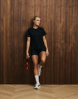 Model wearing Cuera Oncourt Slit Top SS in Black, lifestyle action shot on the padel court