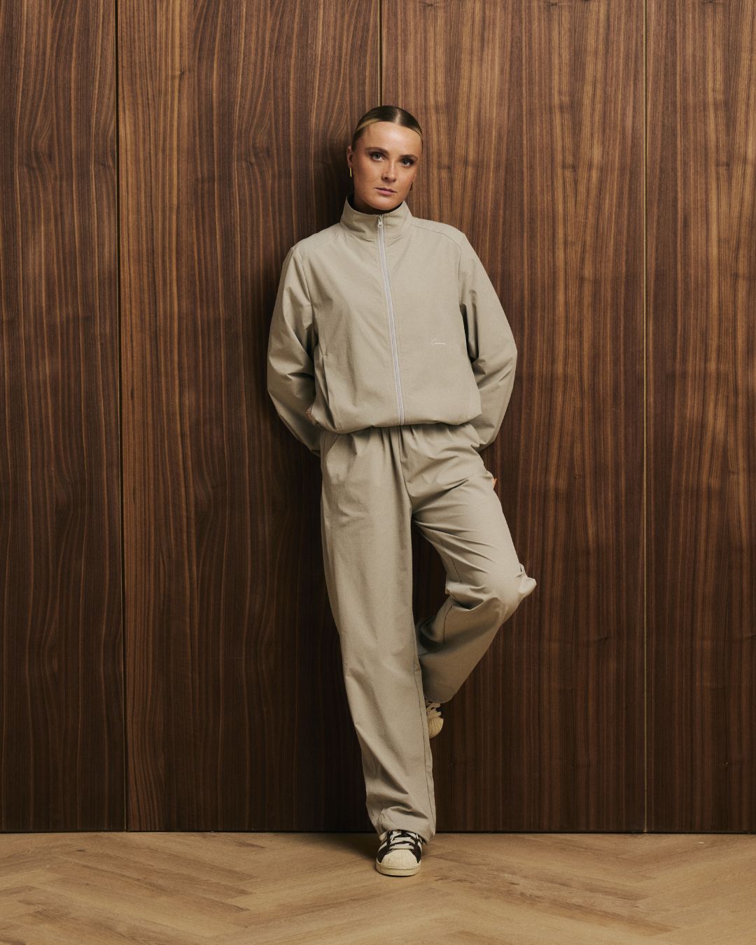 Model wearing Cuera Active Cuera Track Pants in Taupe, lifestyle action shot on the padel court