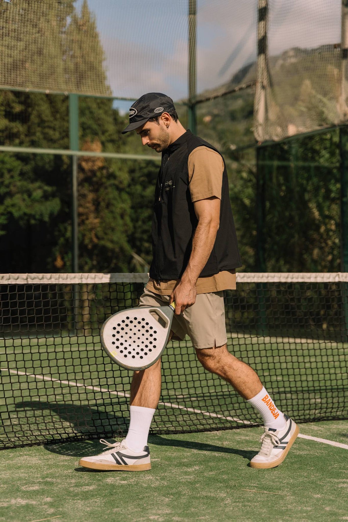 Model wearing Cuera Active Gilet in Black, lifestyle action shot on the padel court