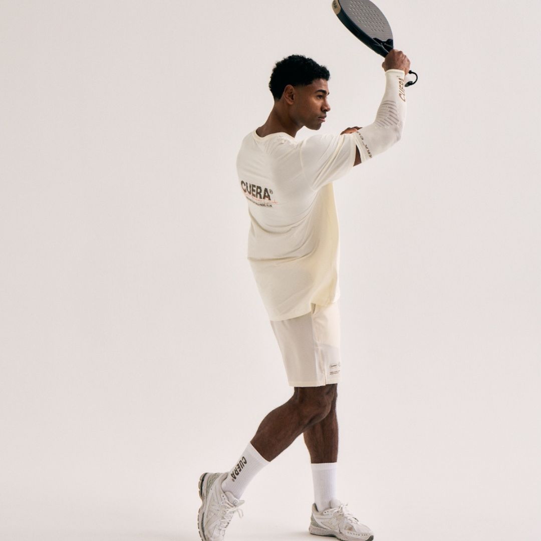 Model wearing Cuera Active Light Weight T-Shirt in Off White/Walnut, lifestyle action shot on the padel court