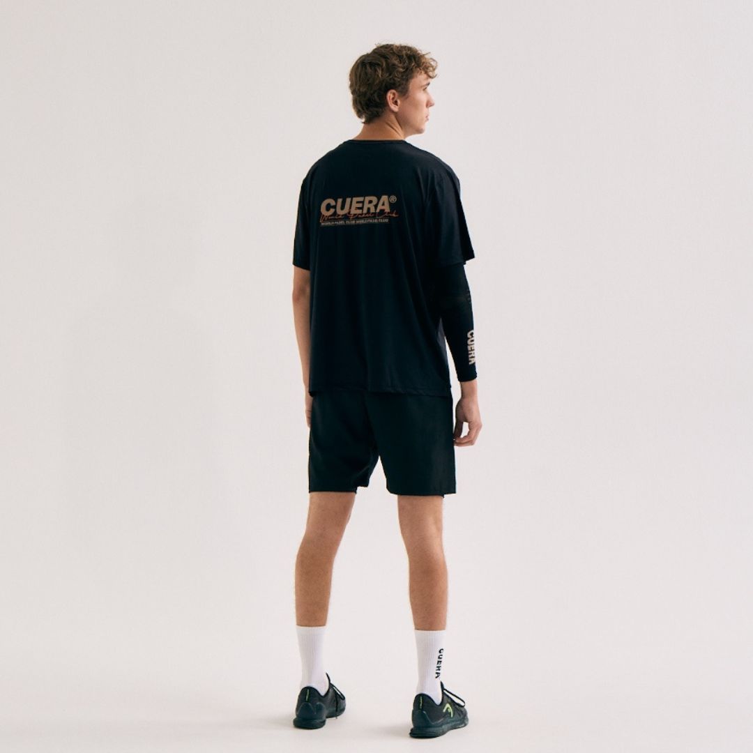Model wearing Cuera Active Light Weight T-Shirt in Black, lifestyle action shot on the padel court