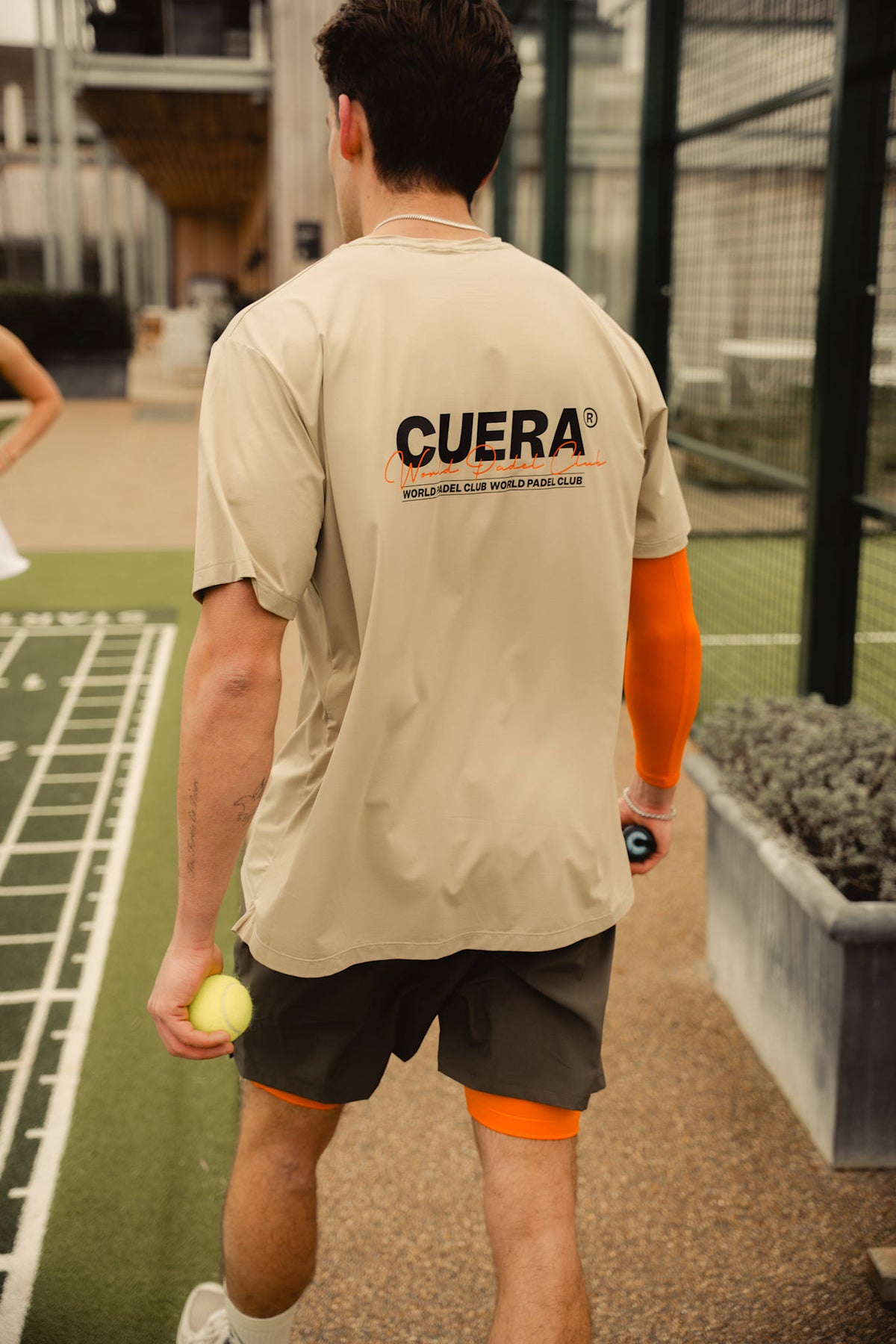 Model wearing Cuera Active Light Weight T-Shirt in Sand, lifestyle action shot on the padel court