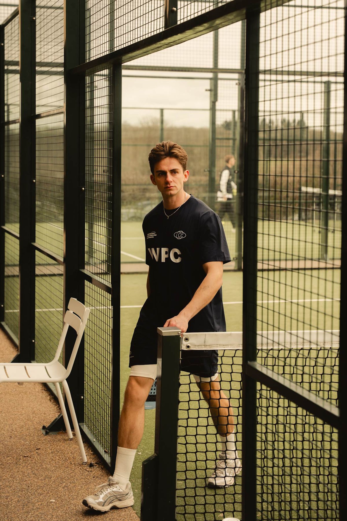 Model wearing Cuera Active WPC Light Weight T-Shirt in Navy, lifestyle action shot on the padel court