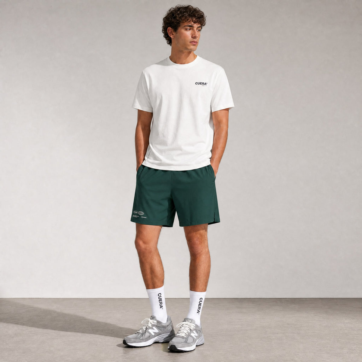 Man wearing Cuera Mens Active Globe Shorts in Court Green, lifestyle action shot on the padel court