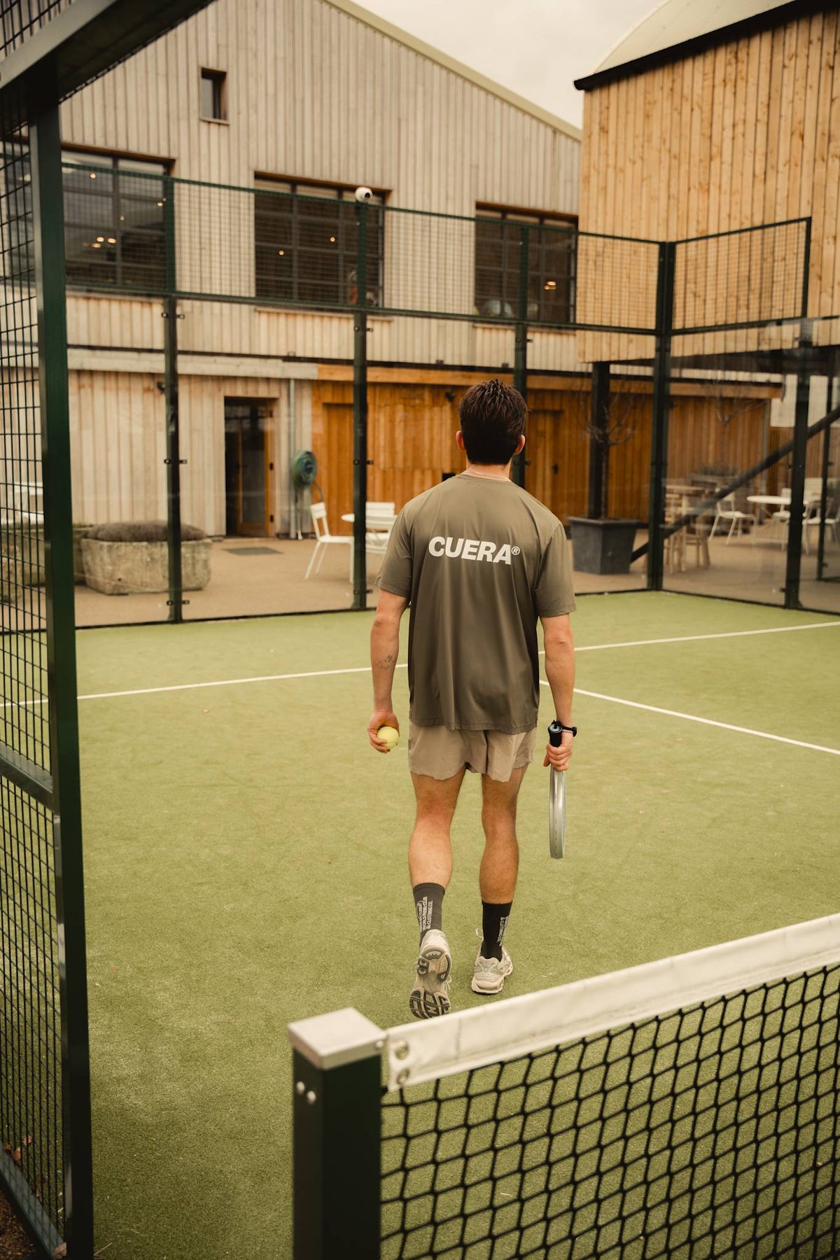 Model wearing Cuera Oncourt Airy Logo T-Shirt in Army, lifestyle action shot on the padel court