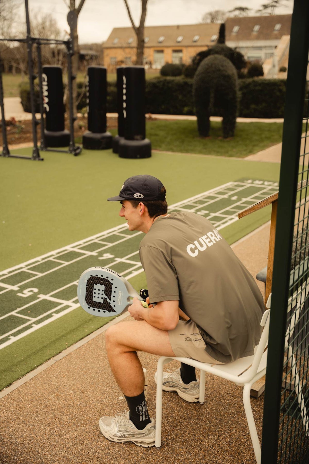 Model wearing Cuera Oncourt Airy Logo T-Shirt in Army, lifestyle action shot on the padel court