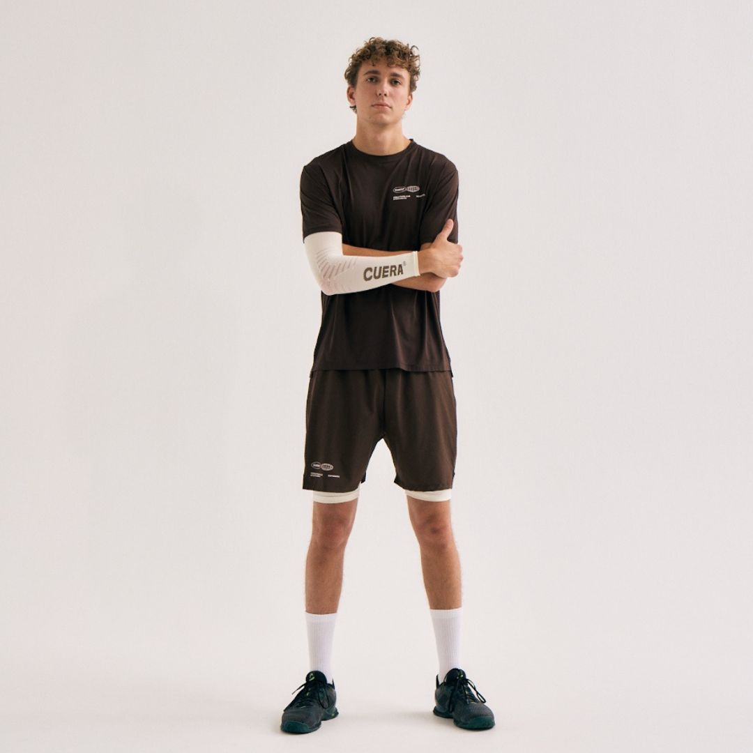 Model wearing Cuera Oncourt Airy Logo T-Shirt in Dark Brown, lifestyle action shot on the padel court