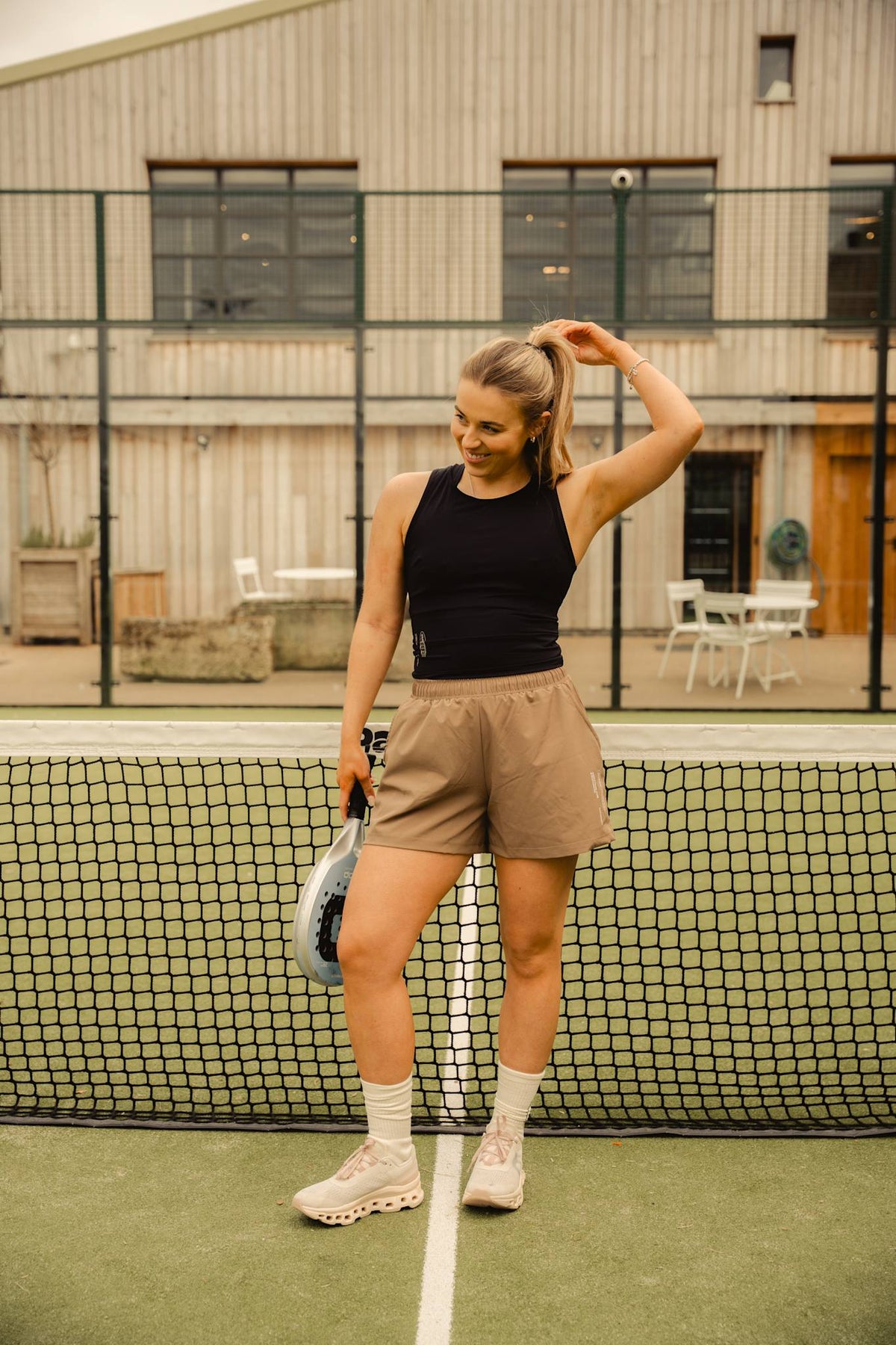 Model wearing Cuera Oncourt Cropped Tank Top in Black, lifestyle action shot on the padel court