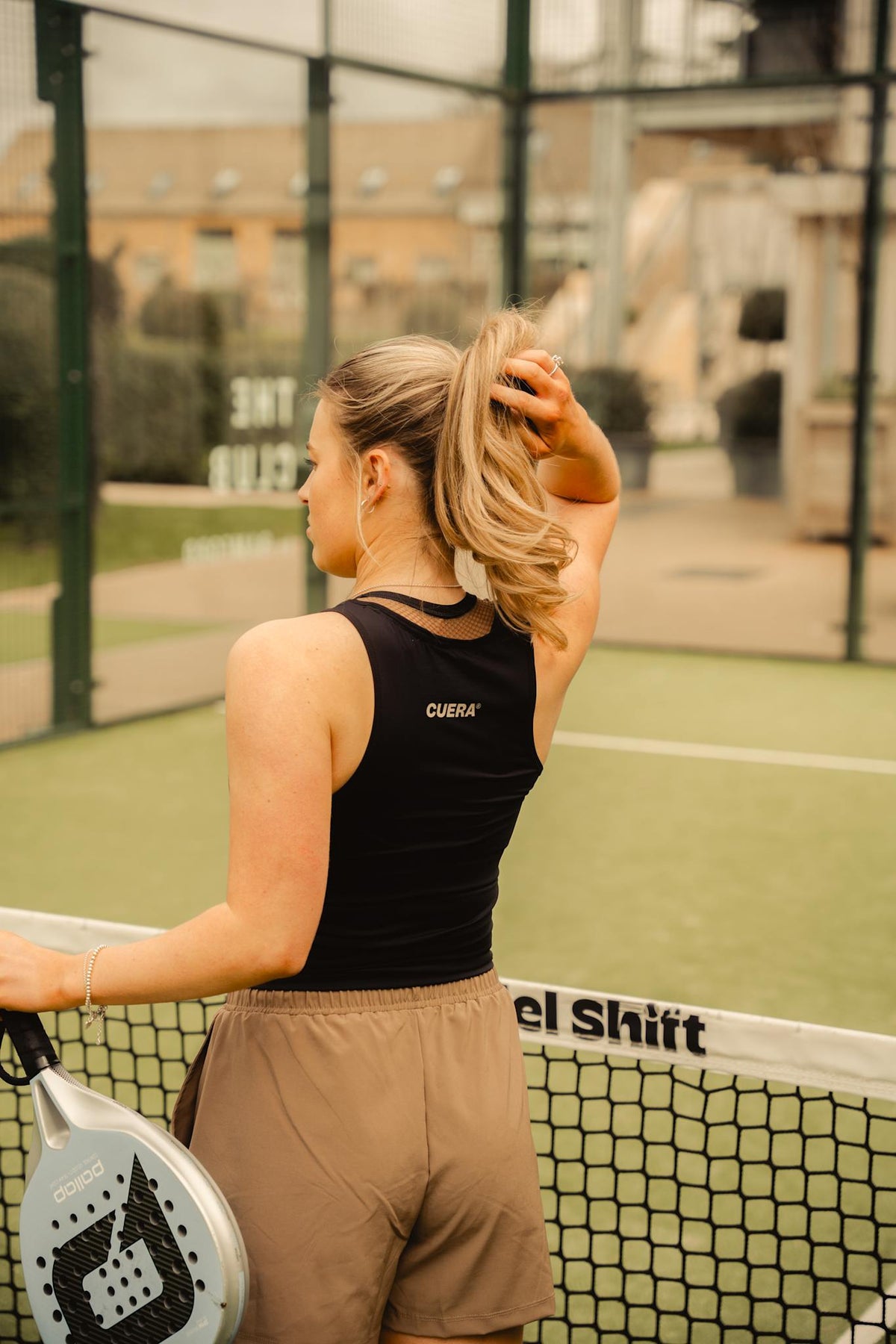 Model wearing Cuera Oncourt Cropped Tank Top in Black, lifestyle action shot on the padel court