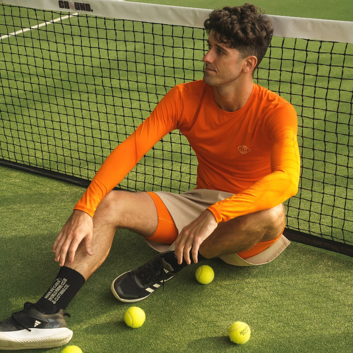 Model wearing Cuera Oncourt LS Layer T-Shirt in Orange, lifestyle action shot on the padel court