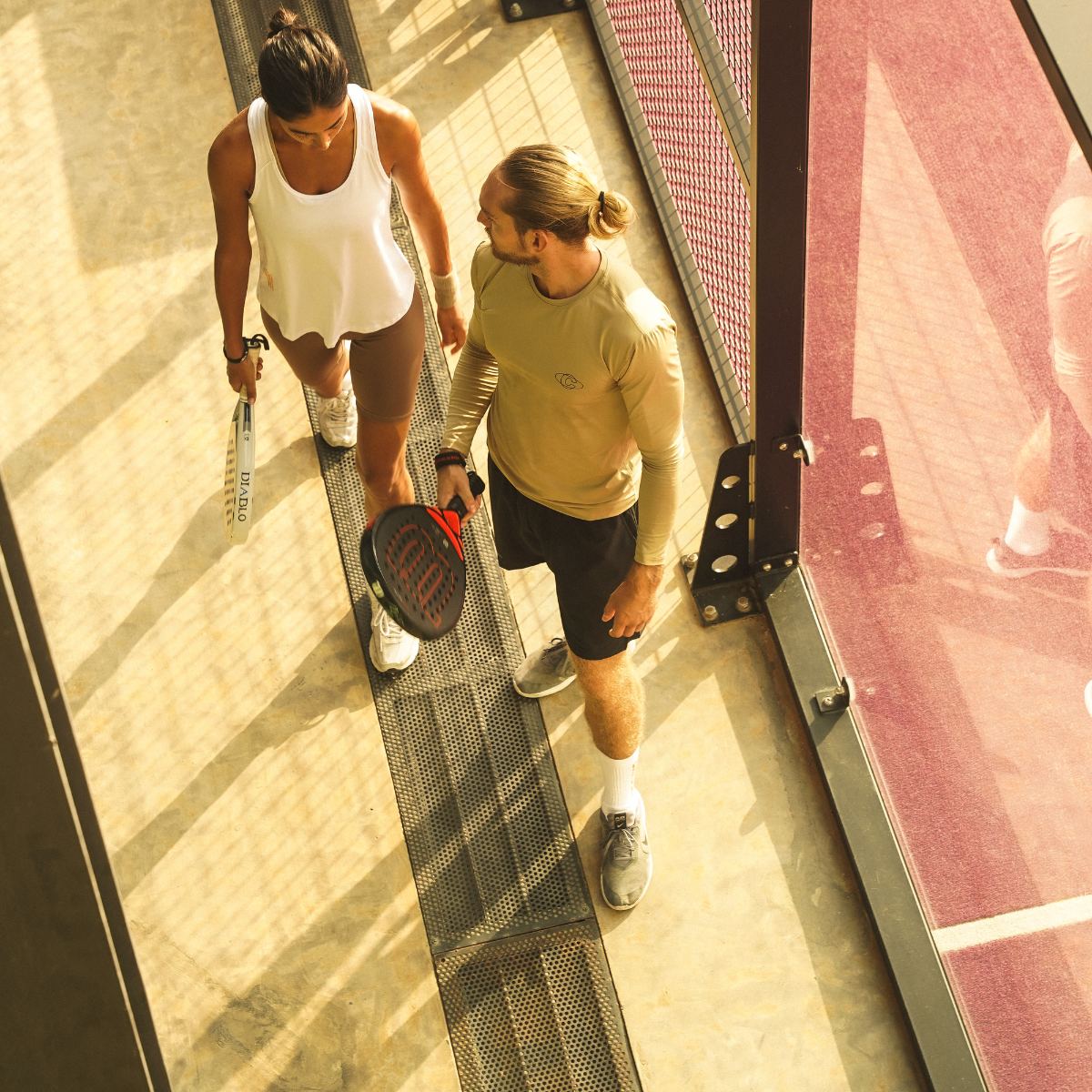 Model wearing Cuera Oncourt LS Layer T-Shirt in Sand, lifestyle action shot on the padel court