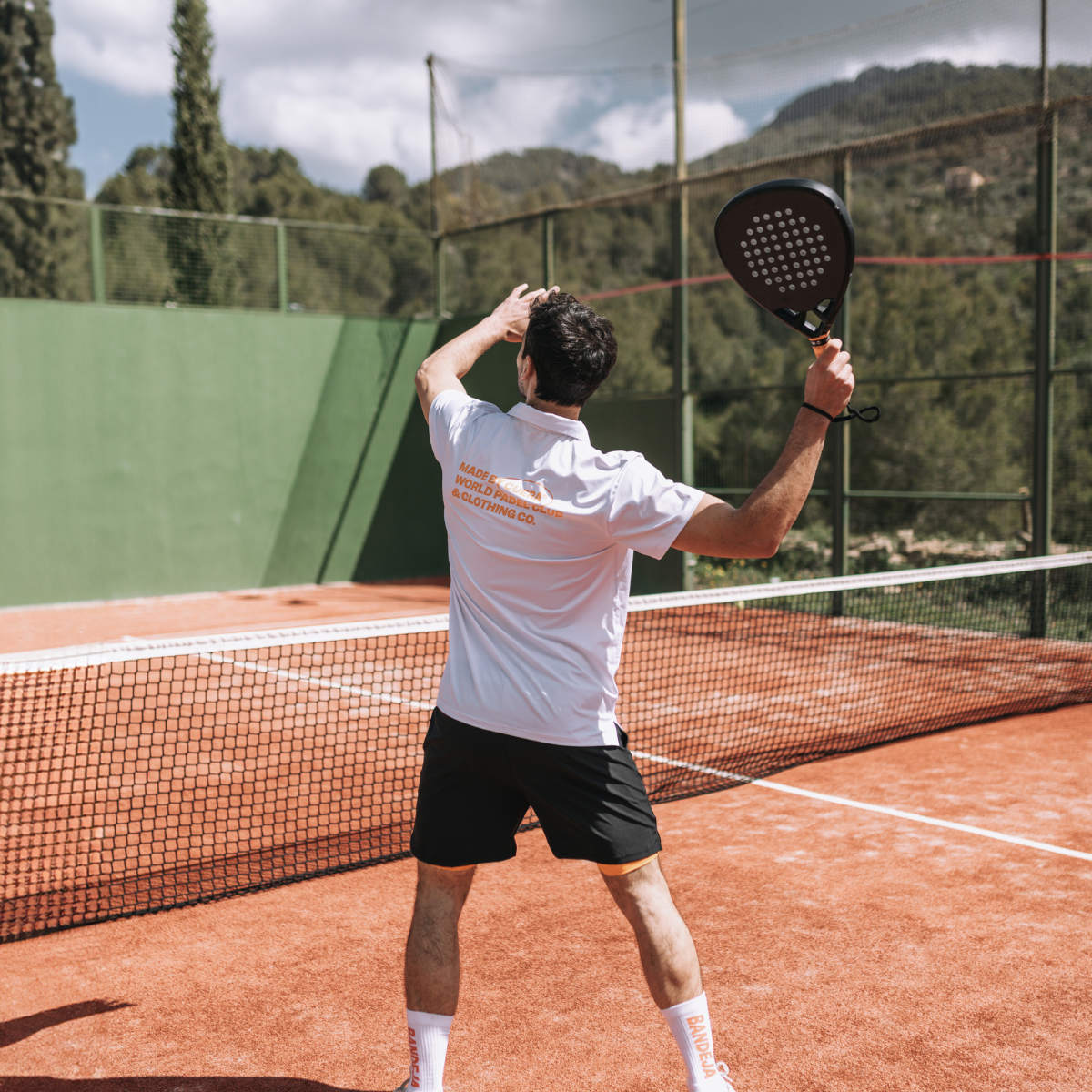 Model wearing Cuera Oncourt Made Polo ss in White, lifestyle action shot on the padel court
